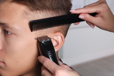 Photo of Professional barber making stylish haircut in salon, closeup