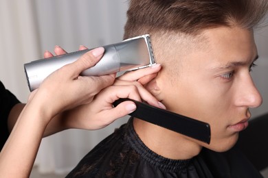 Photo of Professional barber making stylish haircut in salon, closeup