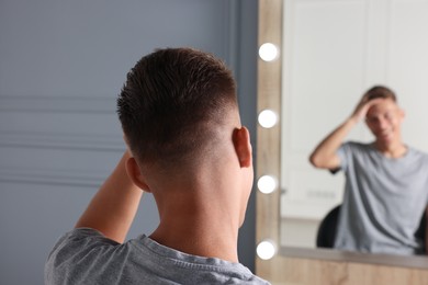 Photo of Man with stylish haircut looking at mirror in salon, back view