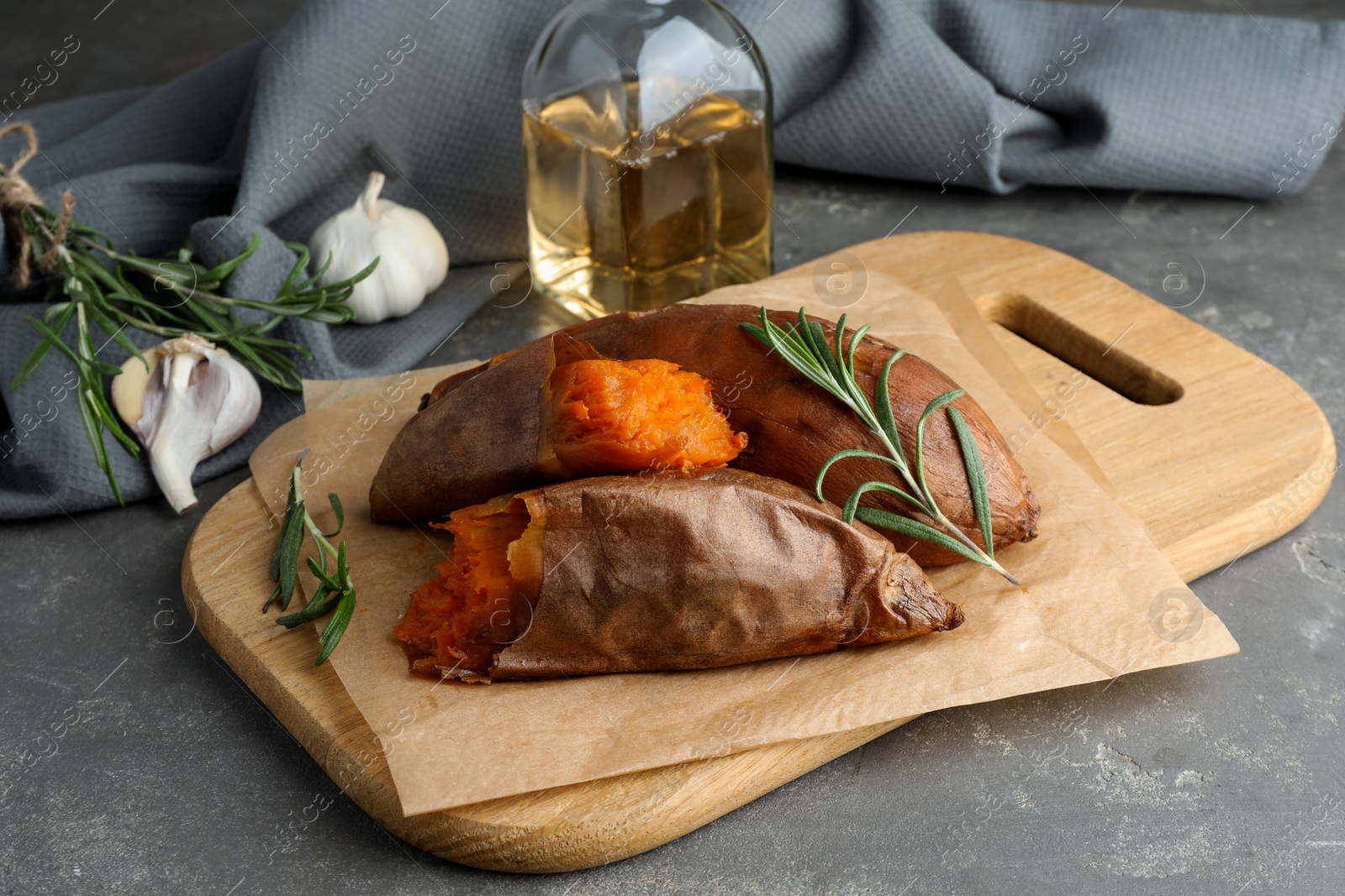 Photo of Tasty cooked sweet potatoes served with rosemary on grey table