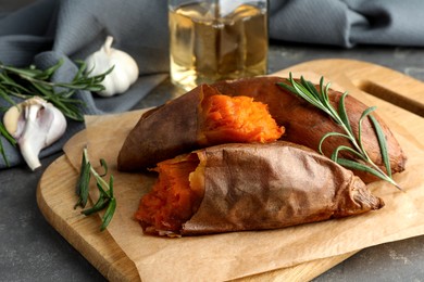 Tasty cooked sweet potatoes served with rosemary on grey table, closeup