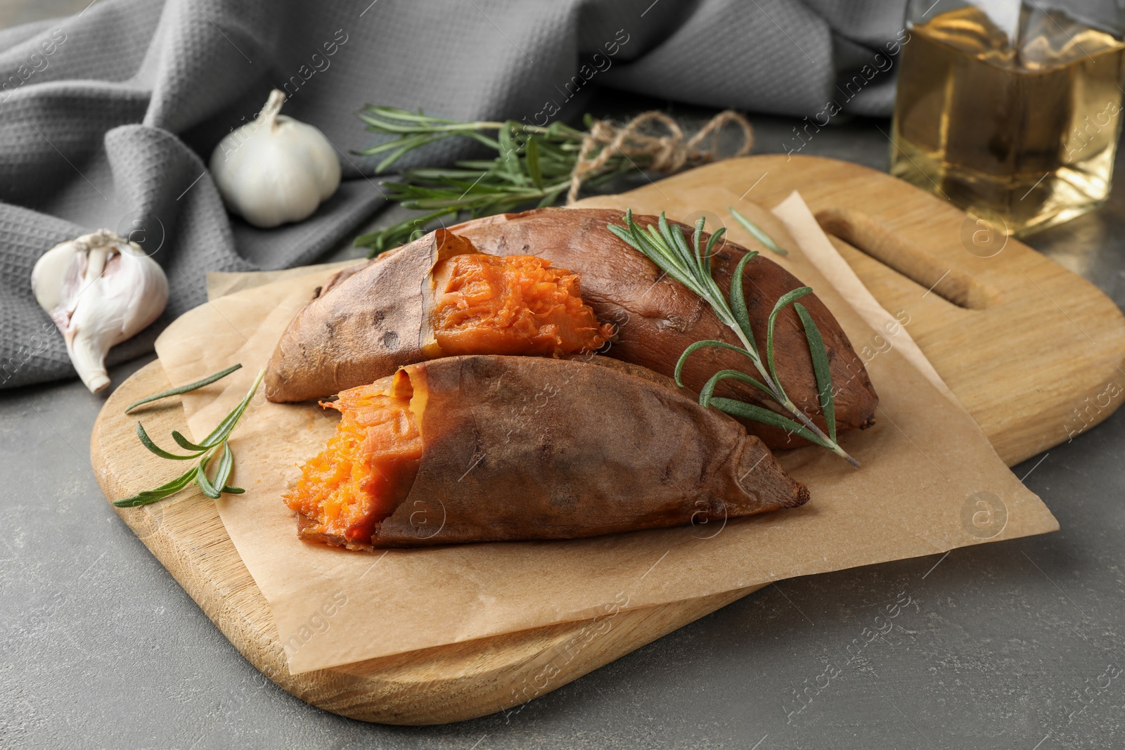 Photo of Tasty cooked sweet potatoes served with rosemary on grey table