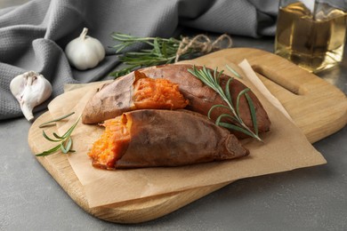 Photo of Tasty cooked sweet potatoes served with rosemary on grey table