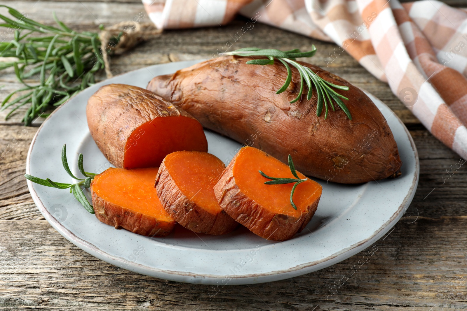 Photo of Tasty cooked sweet potatoes served with rosemary on wooden table