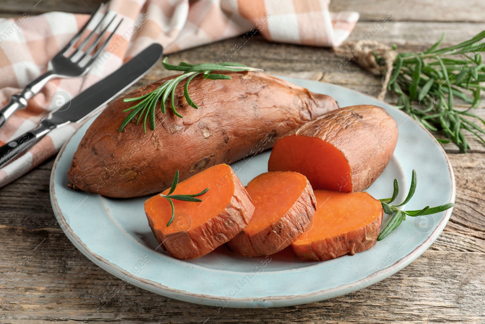 Photo of Tasty cooked sweet potatoes served with rosemary on wooden table