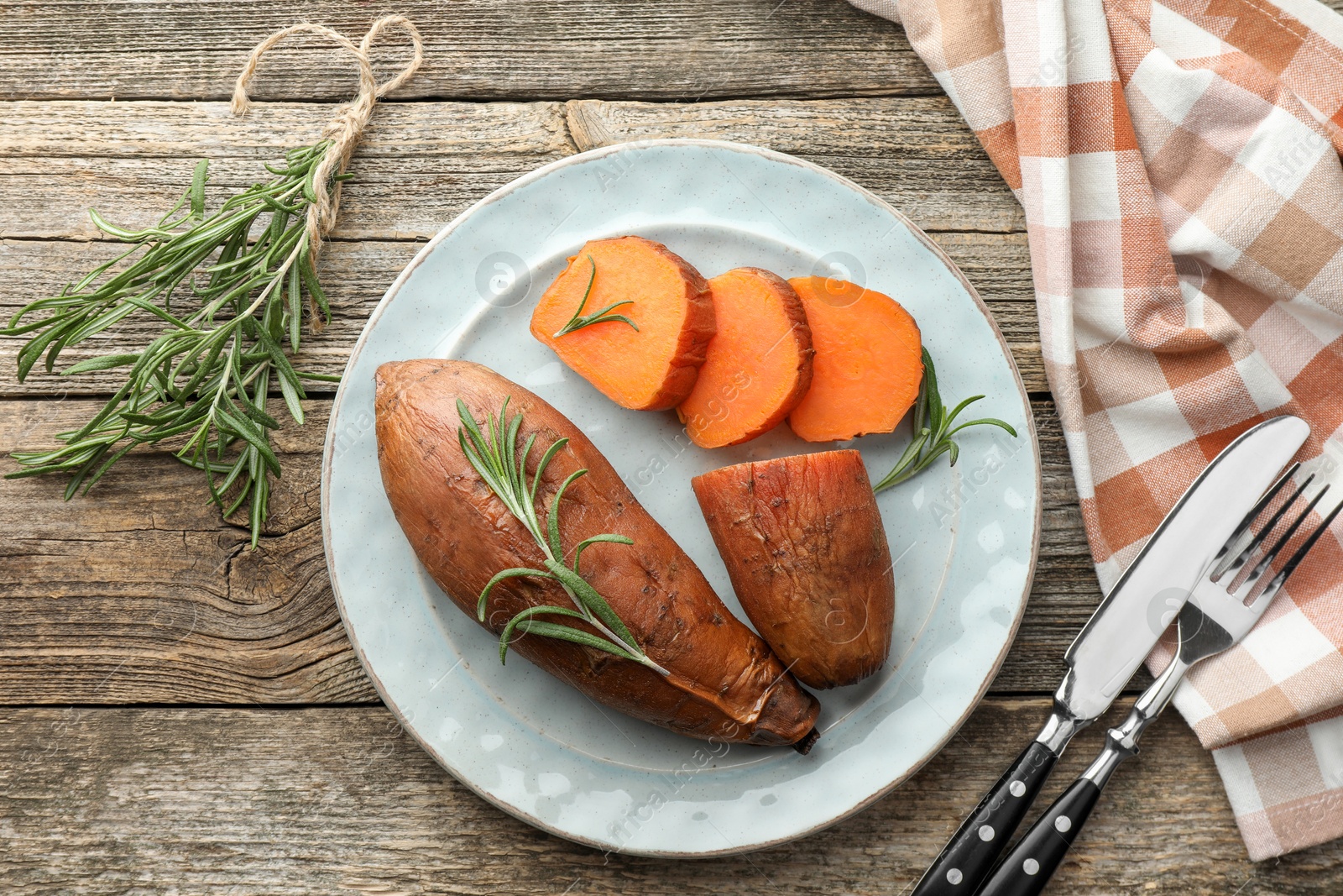 Photo of Tasty cooked sweet potatoes served with rosemary and cutlery on wooden table, flat lay