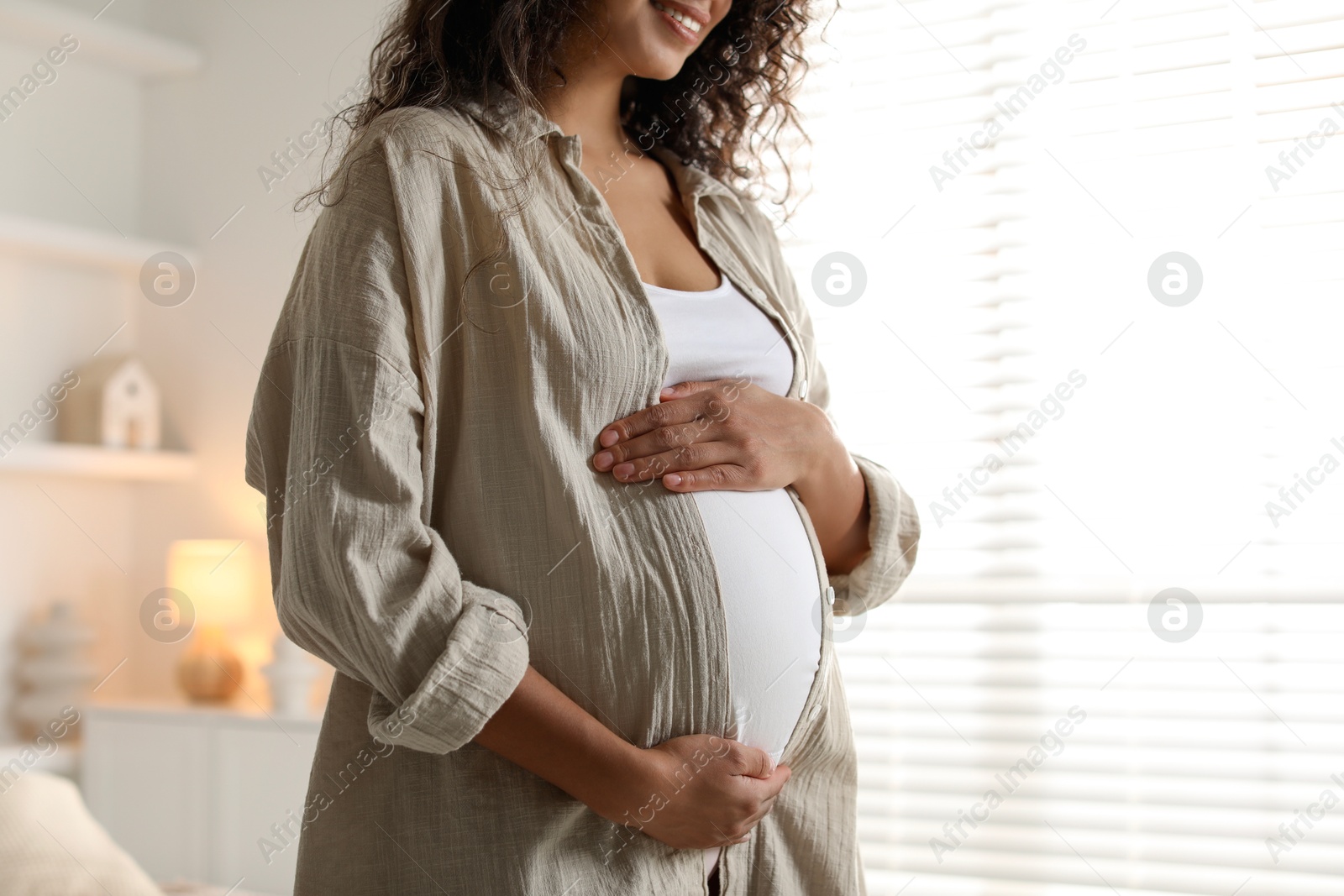 Photo of Pregnant woman near window at home, closeup