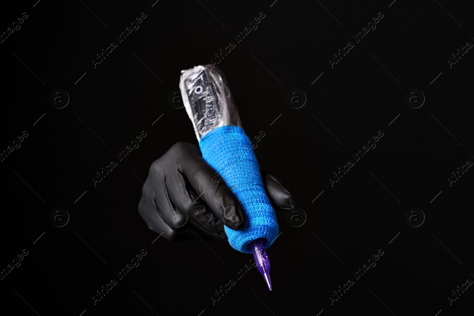 Photo of Professional artist in gloves holding tattoo machine on black background, closeup