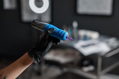 Photo of Professional artist in gloves with tattoo machine in salon, closeup. Space for text