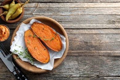 Photo of Tasty cooked sweet potato served with thyme and sauce on wooden table, top view. Space for text