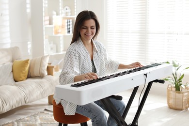 Photo of Smiling woman playing synthesizer at home. Electronic musical instrument