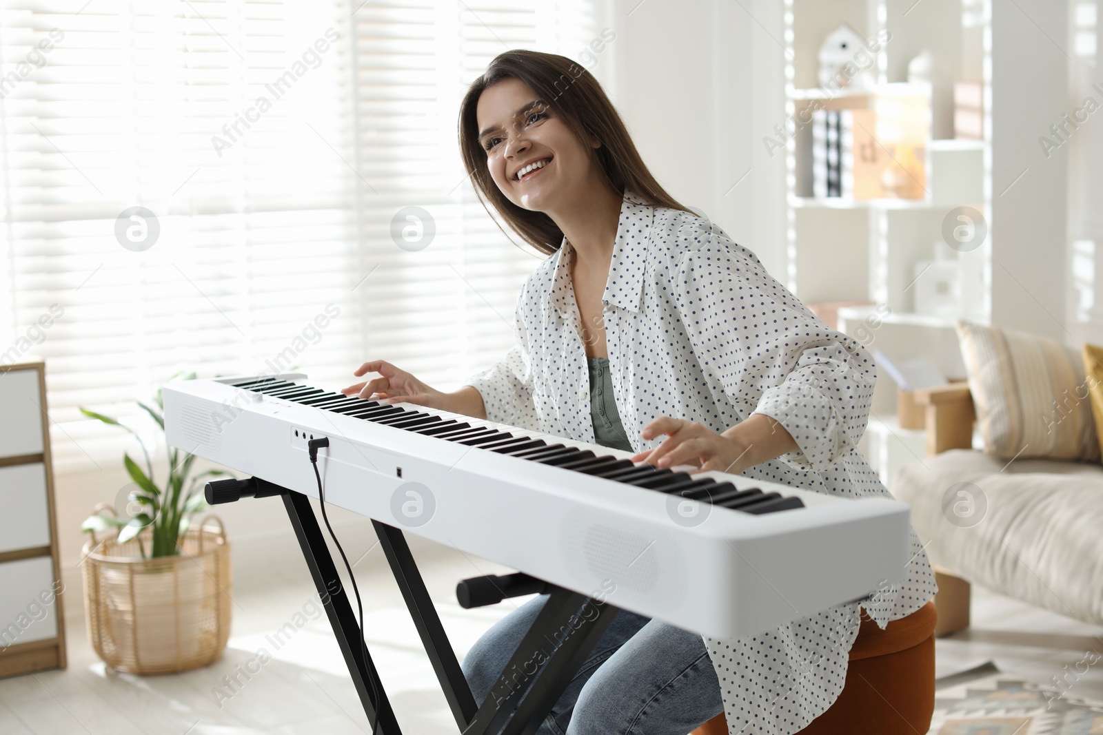 Photo of Smiling woman playing synthesizer at home. Electronic musical instrument