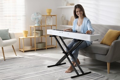 Photo of Smiling woman playing synthesizer at home. Electronic musical instrument