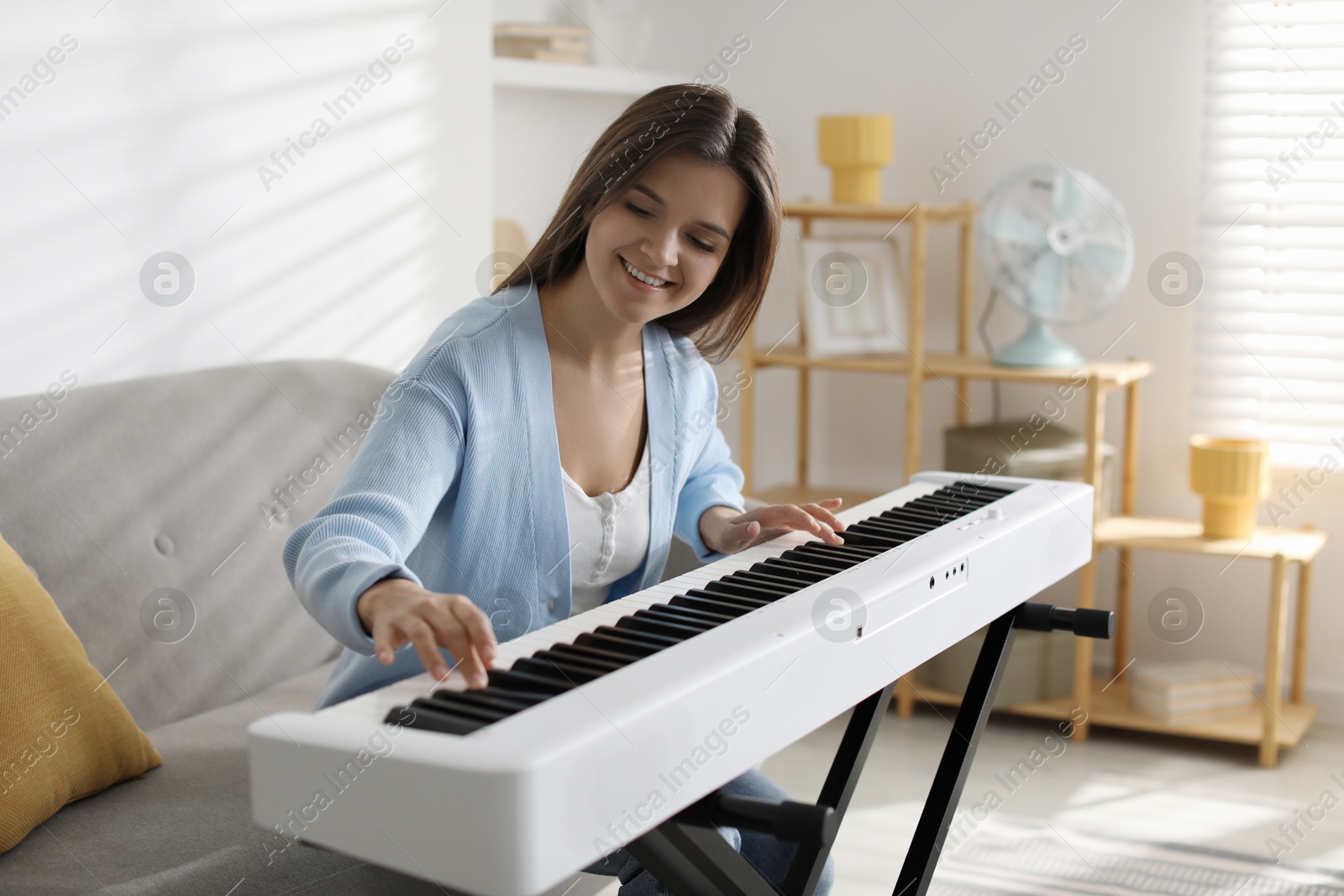 Photo of Smiling woman playing synthesizer at home. Electronic musical instrument