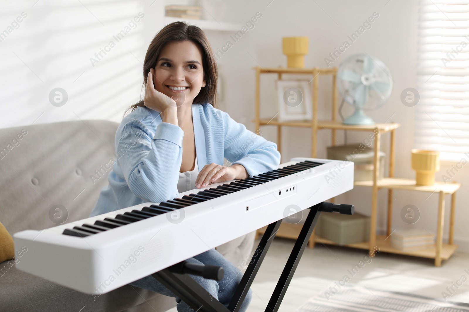 Photo of Beautiful woman sitting on sofa near synthesizer at home. Space for text