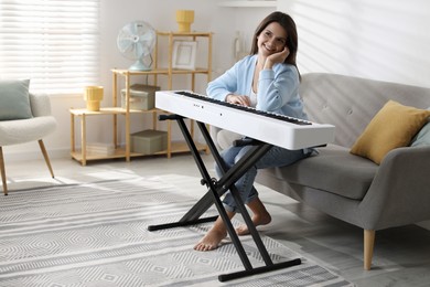 Photo of Beautiful woman sitting on sofa near synthesizer at home