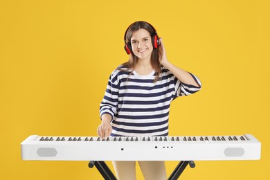 Photo of Smiling woman in headphones playing synthesizer on orange background