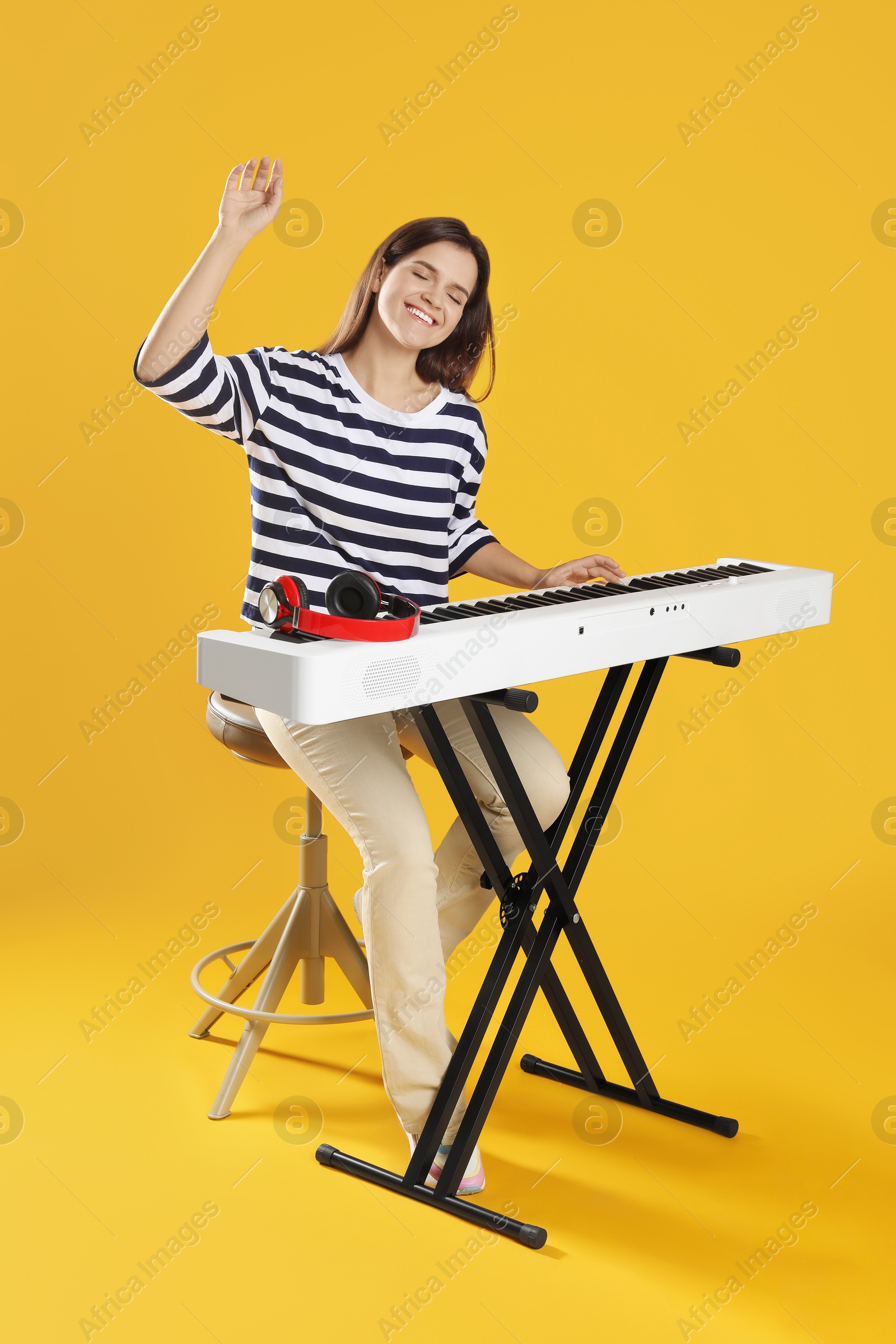 Photo of Smiling woman playing synthesizer on orange background