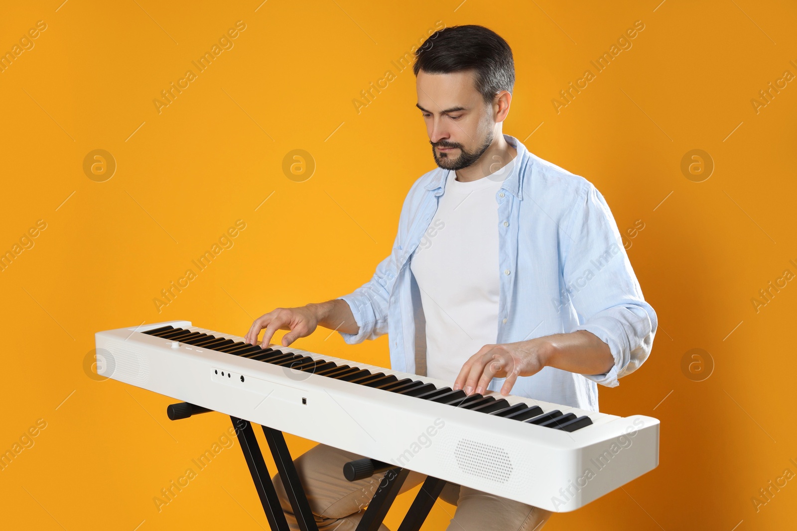 Photo of Bearded man playing synthesizer on orange background