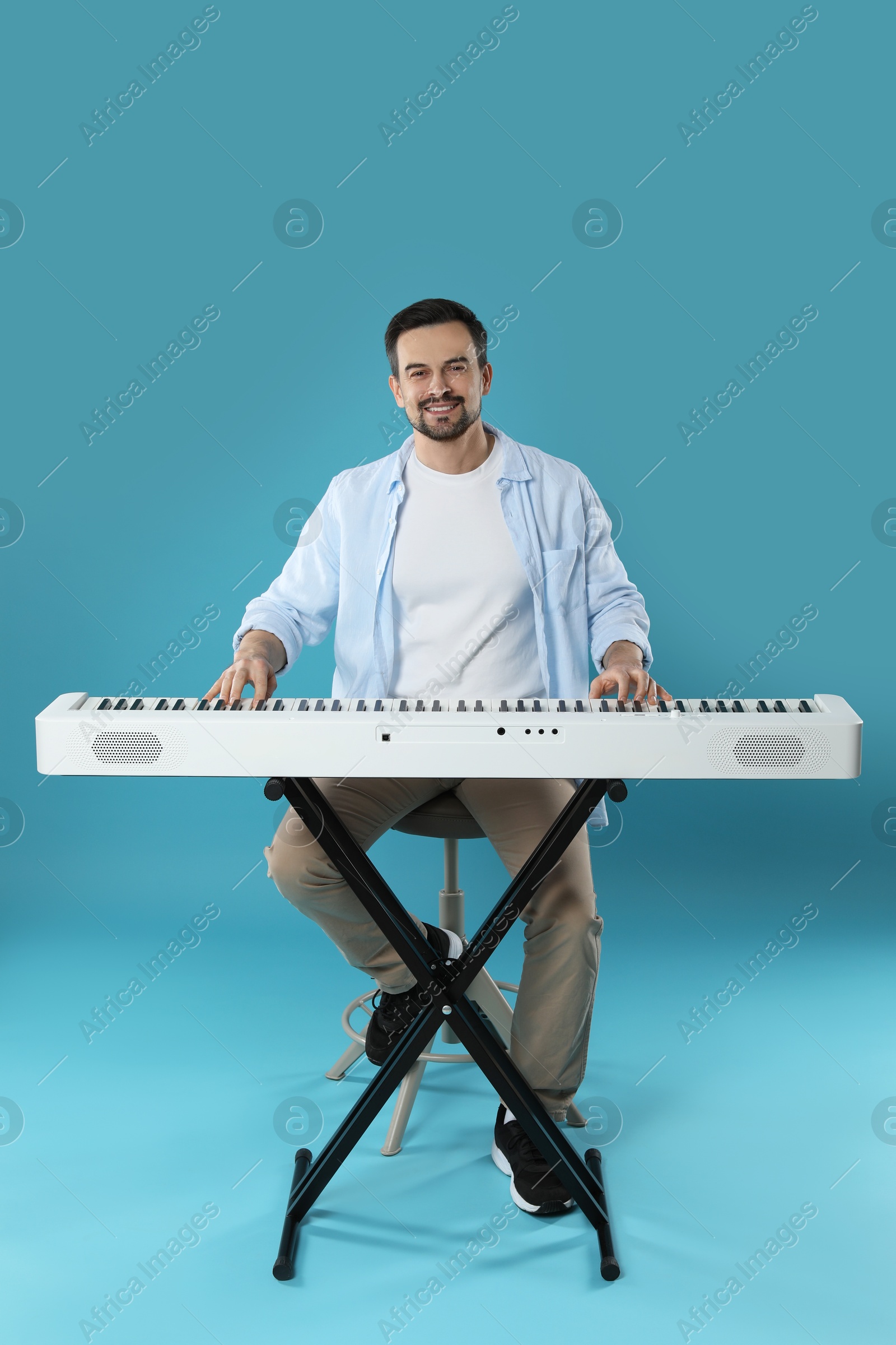 Photo of Smiling man playing synthesizer on light blue background