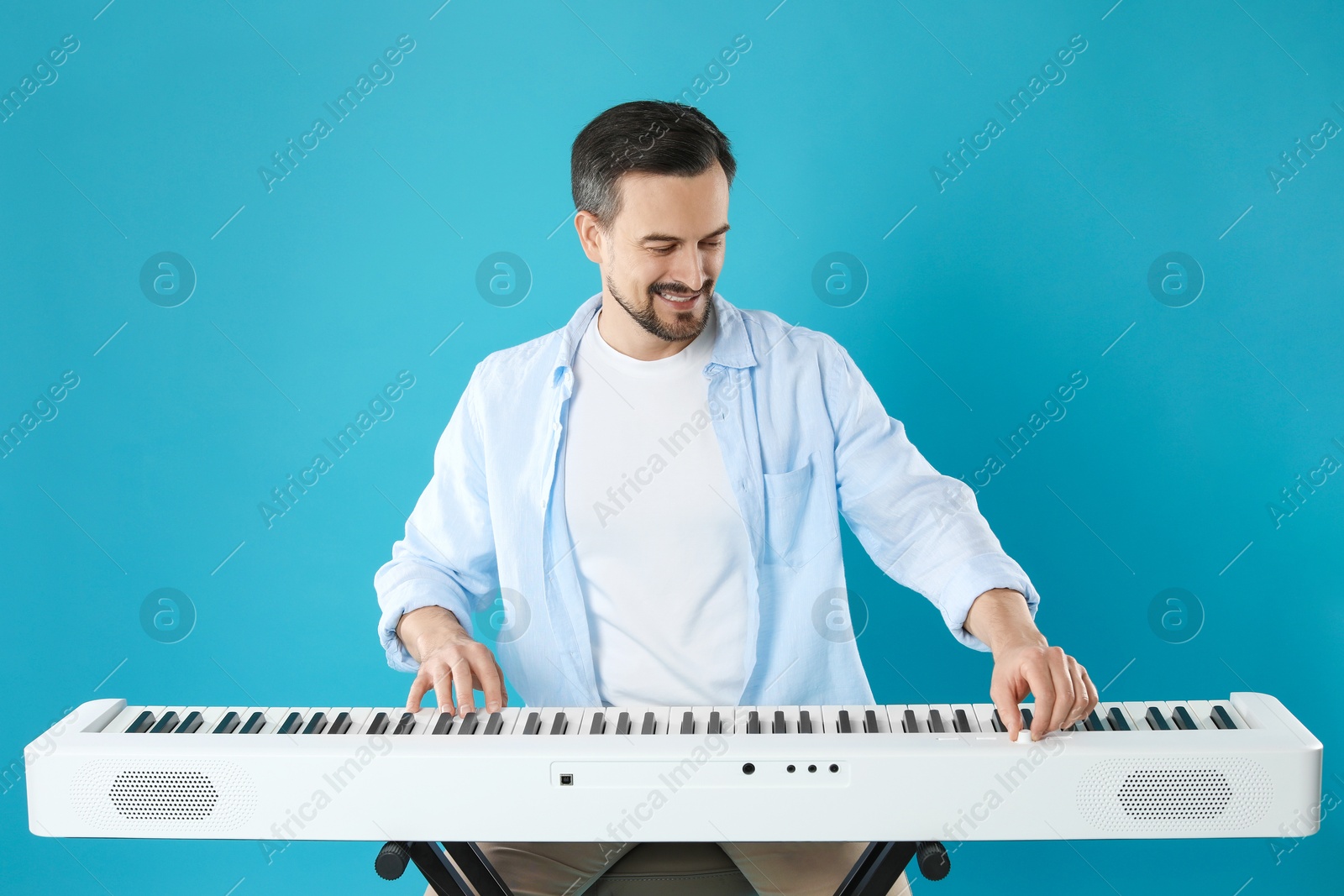 Photo of Smiling man playing synthesizer on light blue background