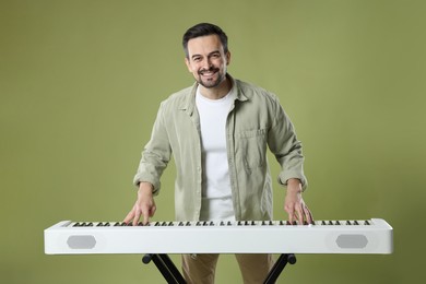 Photo of Smiling man playing synthesizer on olive background