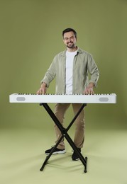 Photo of Smiling man playing synthesizer on olive background