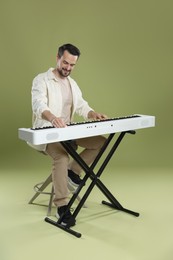 Photo of Smiling man playing synthesizer on olive background