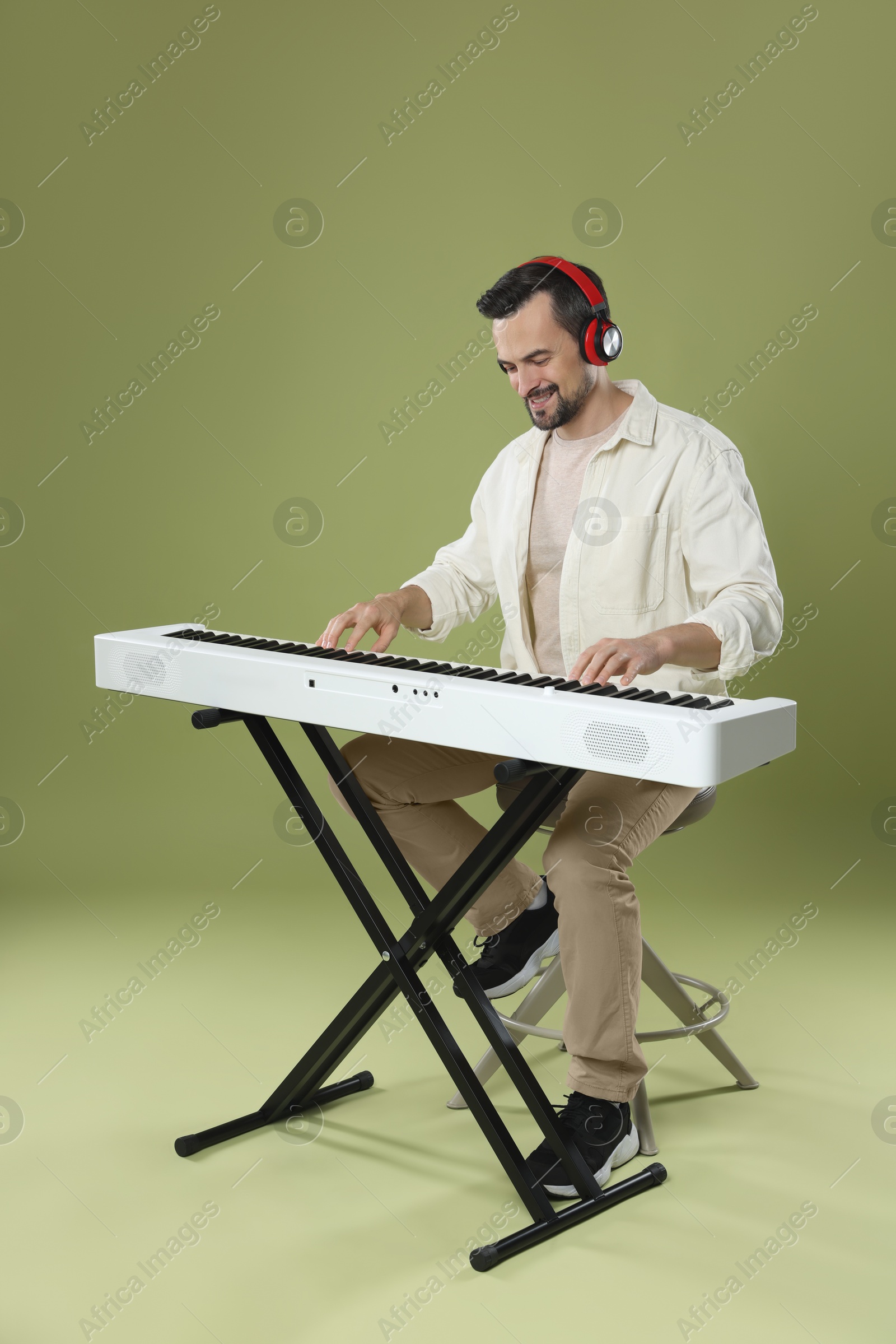 Photo of Smiling man in headphones playing synthesizer on olive background