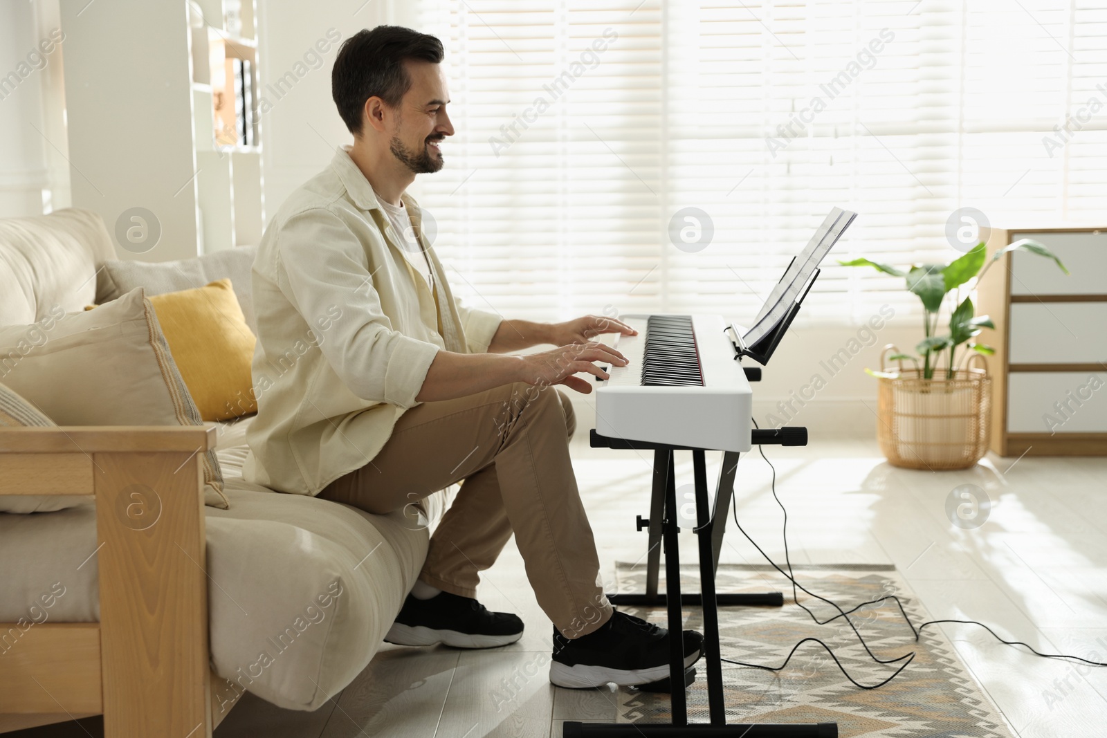 Photo of Bearded man playing synthesizer at home. Electronic musical instrument