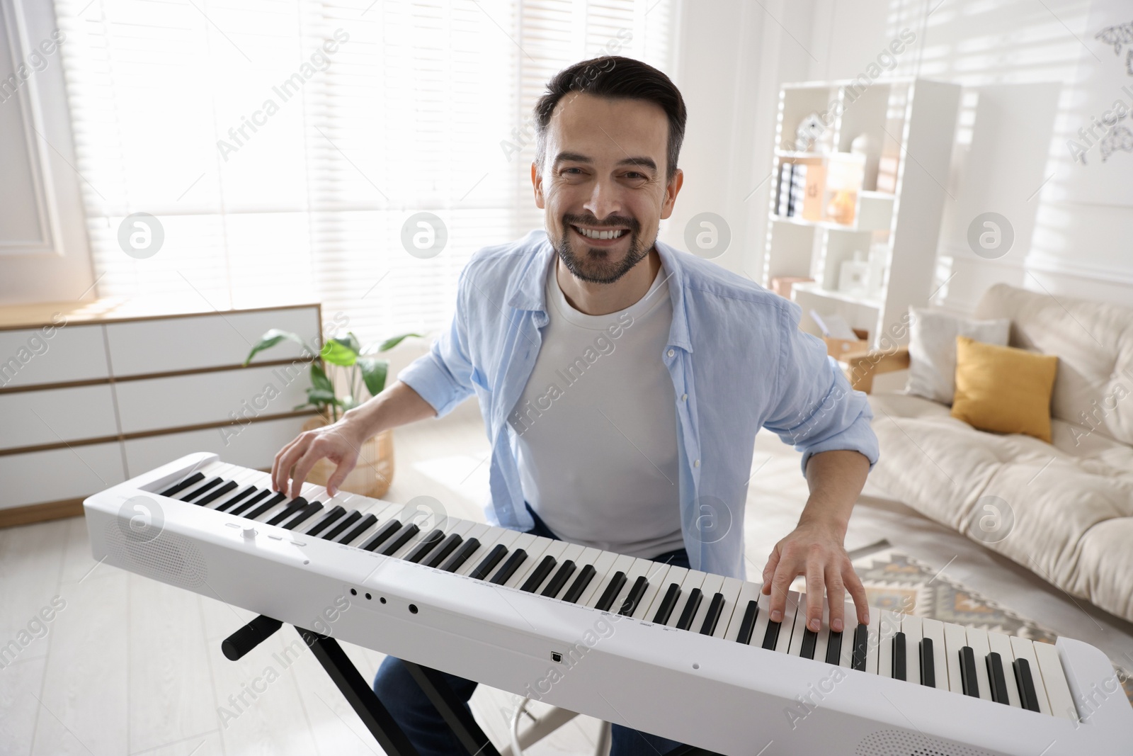 Photo of Smiling man playing synthesizer at home. Electronic musical instrument