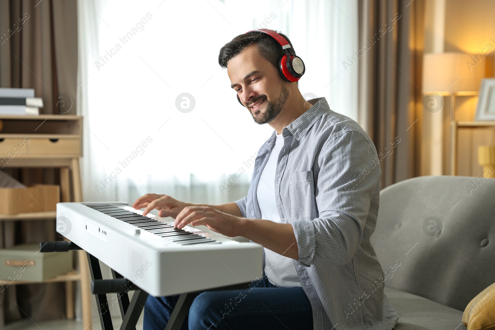 Photo of Smiling man in headphones playing synthesizer at home