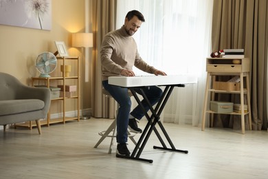 Photo of Smiling man playing synthesizer at home. Electronic musical instrument