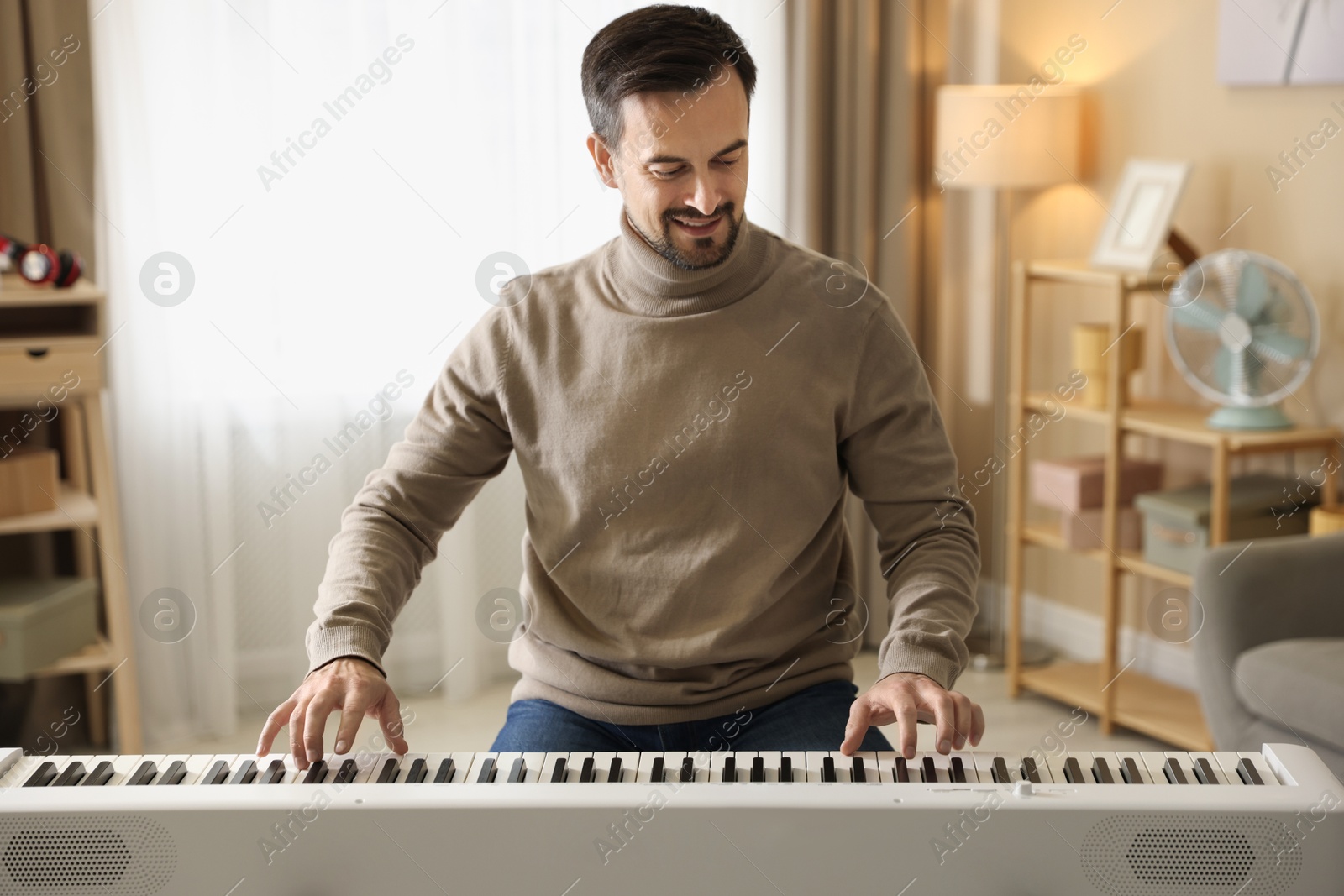 Photo of Smiling man playing synthesizer at home. Electronic musical instrument