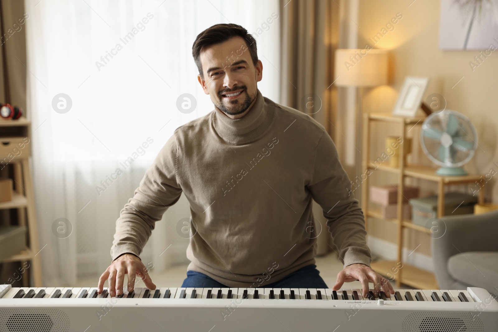 Photo of Smiling man playing synthesizer at home. Electronic musical instrument