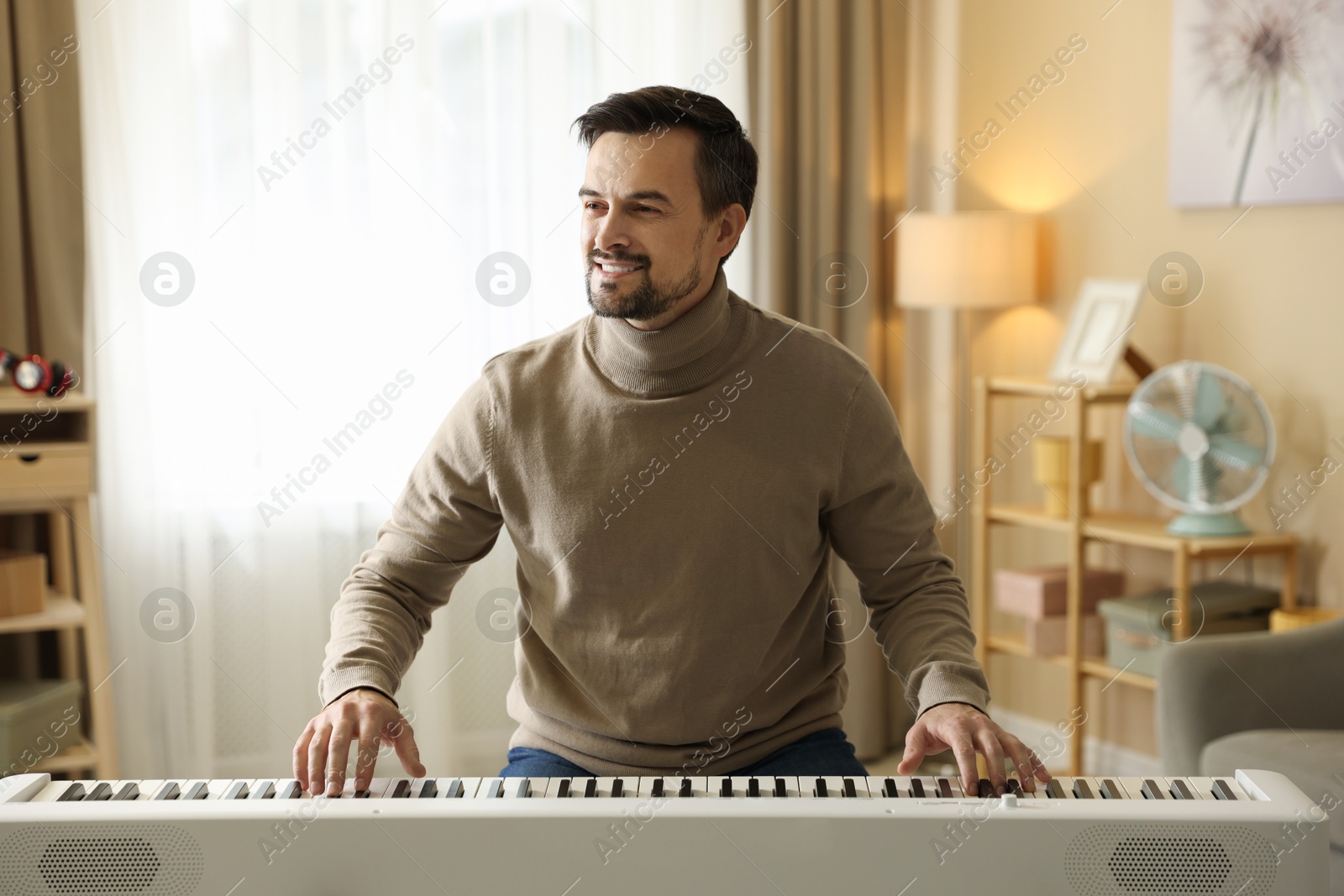 Photo of Smiling man playing synthesizer at home. Electronic musical instrument