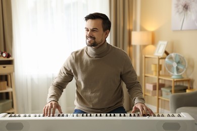 Photo of Smiling man playing synthesizer at home. Electronic musical instrument