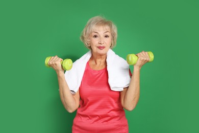 Photo of Senior woman exercising with dumbbells and towel on green background