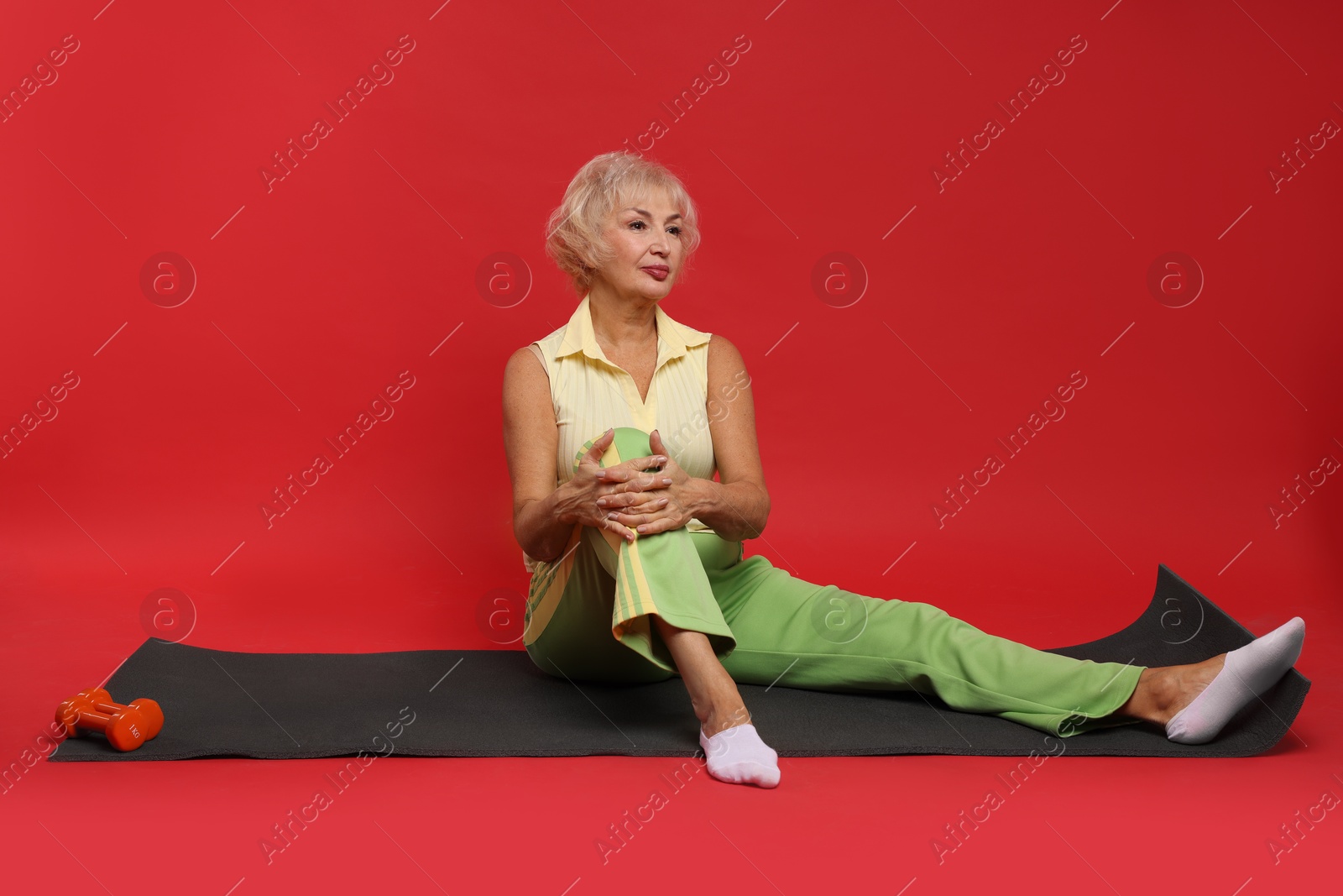 Photo of Senior woman exercising with fitness mat on red background