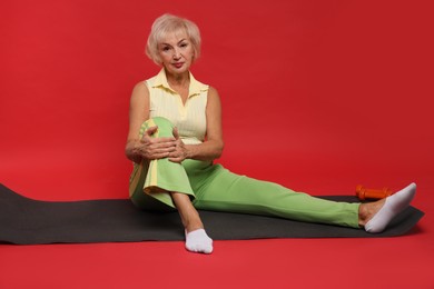 Photo of Senior woman exercising with fitness mat on red background