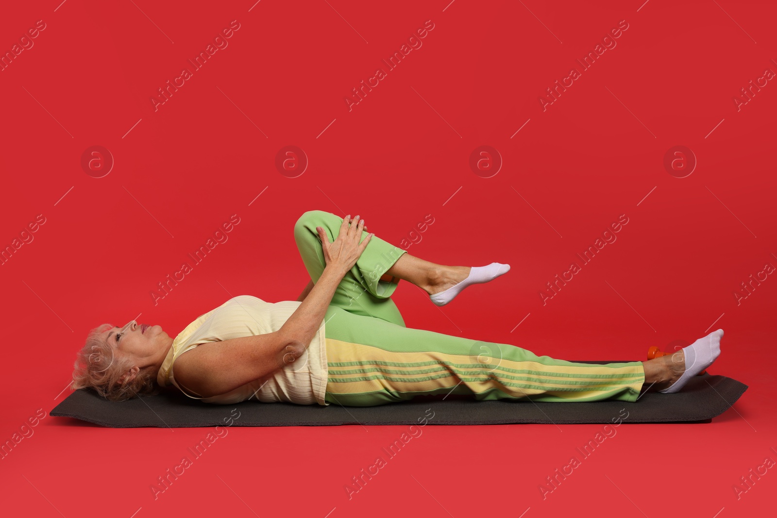 Photo of Senior woman exercising with fitness mat on red background. Space for text