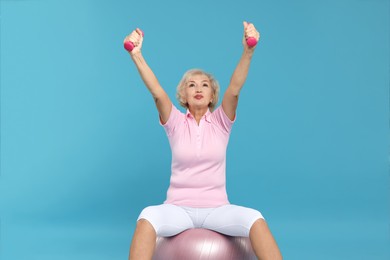 Photo of Senior woman exercising with fitness ball and dumbbells on light blue background