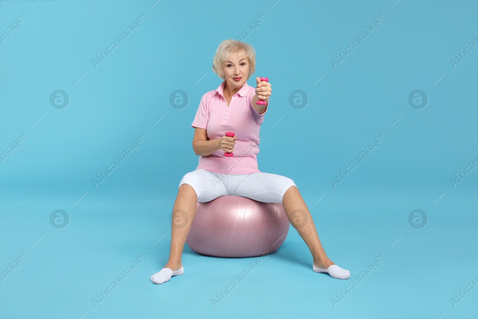 Photo of Senior woman exercising with fitness ball and dumbbells on light blue background