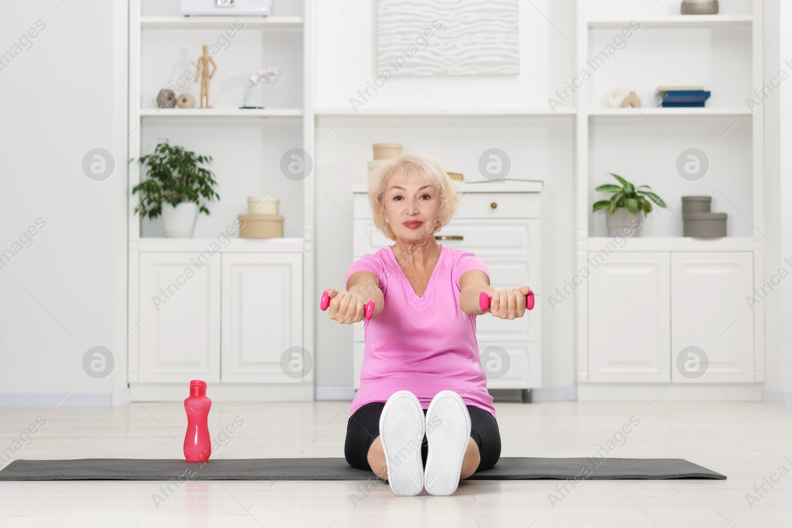 Photo of Senior woman exercising with fitness mat and dumbbells at home