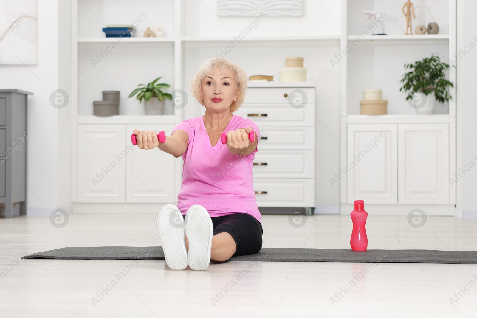 Photo of Senior woman exercising with fitness mat and dumbbells at home