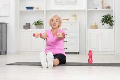 Photo of Senior woman exercising with fitness mat and dumbbells at home