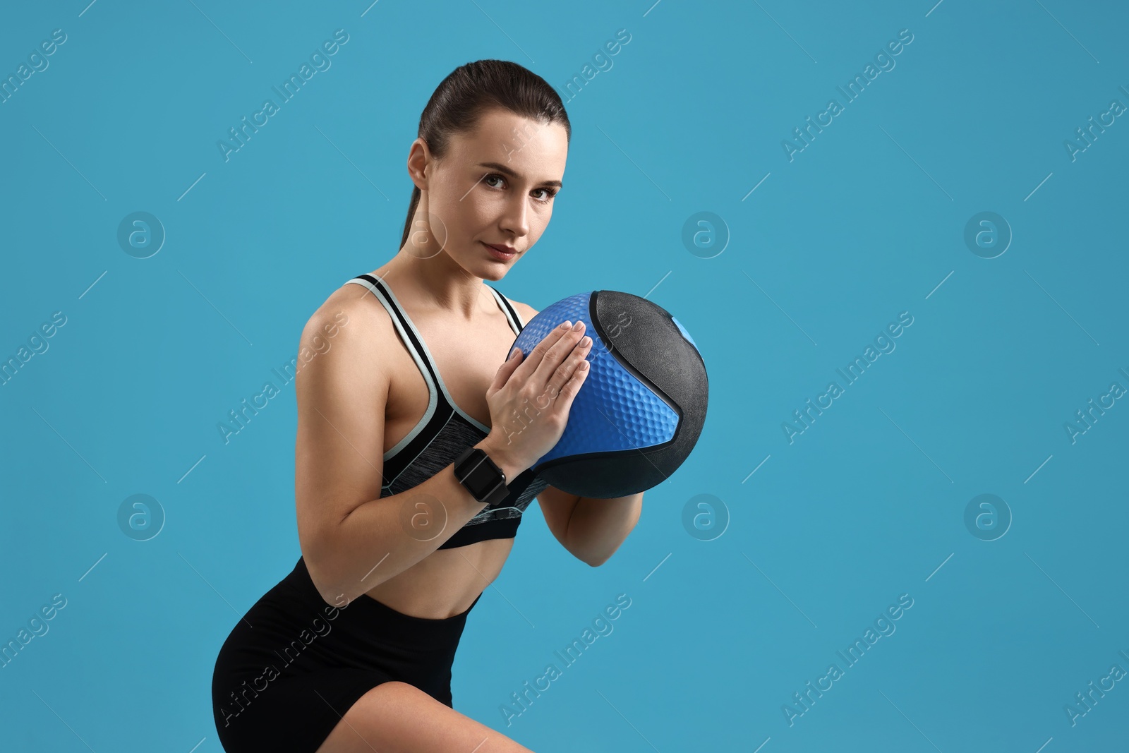 Photo of Woman in gym clothes doing exercise with medicine ball on light blue background, space for text