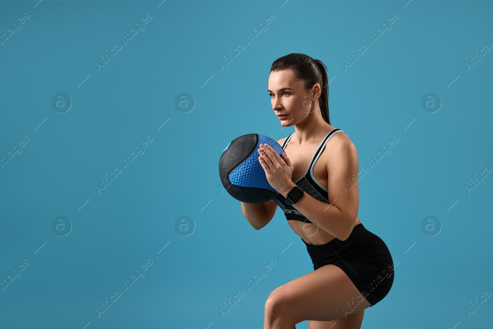 Photo of Woman in gym clothes doing exercise with medicine ball on light blue background, space for text