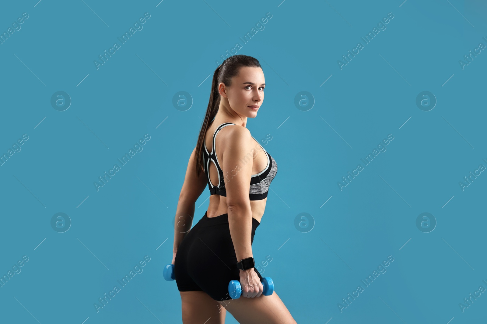 Photo of Woman in gym clothes exercising with dumbbells on light blue background