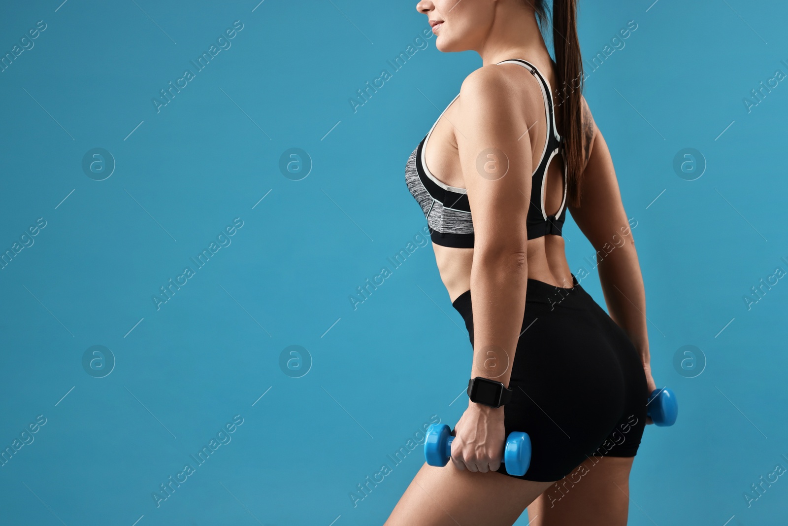 Photo of Woman in gym clothes exercising with dumbbells on light blue background, closeup. Space for text